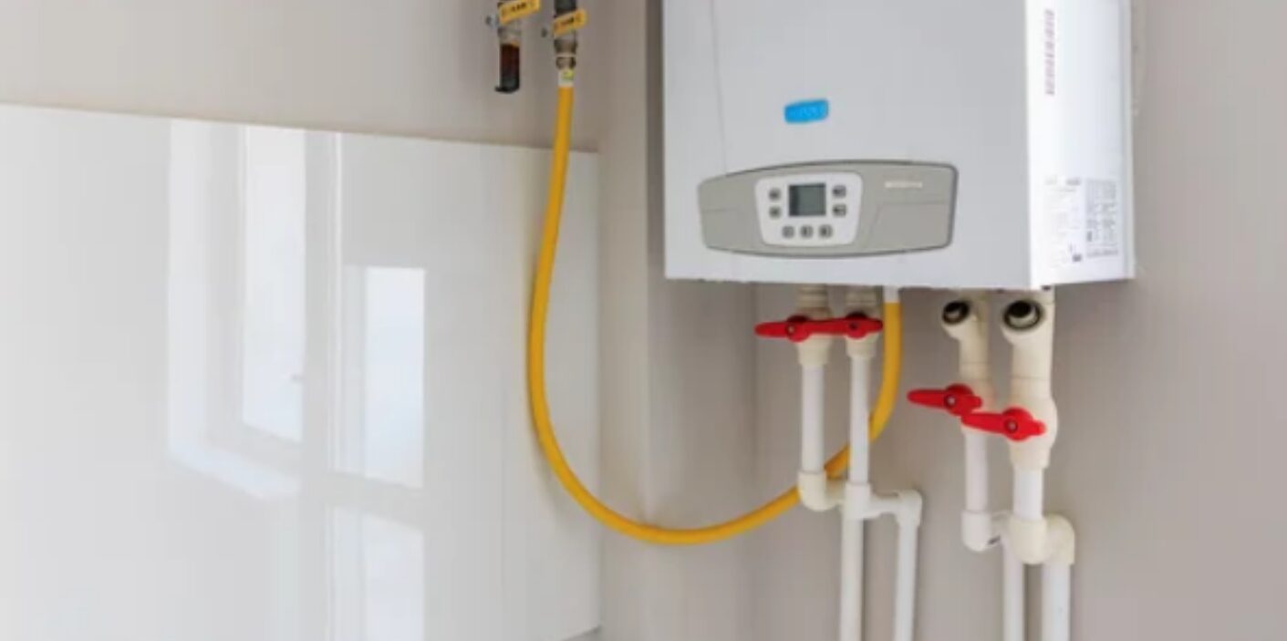 Modern wall-mounted gas water heater with yellow gas line and shut-off valves – water heater summer tips