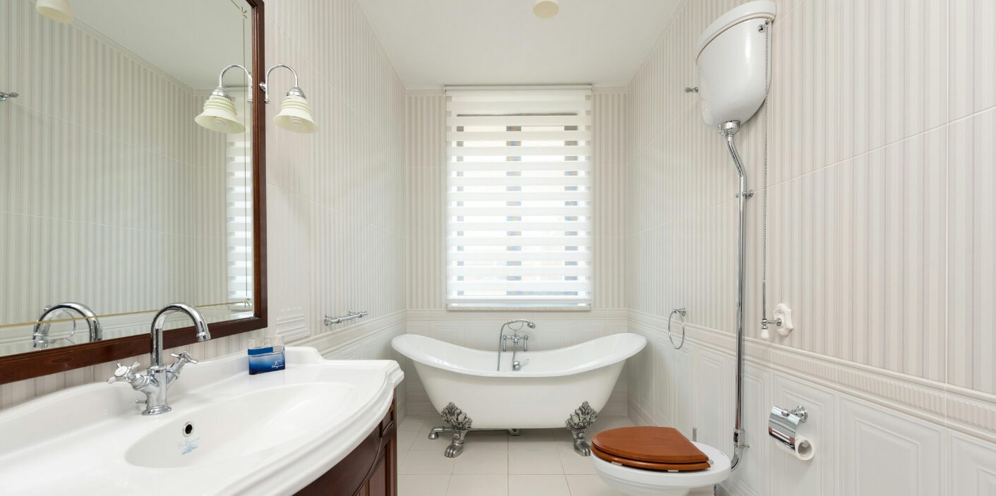 Clean bathroom with a white clawfoot tub and sink, ready for summer plumbing tips.