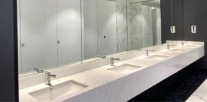 A row of modern sinks with silver faucets and a marble countertop in a commercial bathroom, symbolizing the need for professional plumbing maintenance.