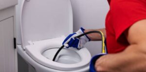 A plumber's gloved hand uses a drain snake to fix a clogged toilet.