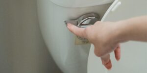 A hand pushing the flush lever of a toilet, illustrating a user interacting with a fixture prone to Common Toilet Problems.