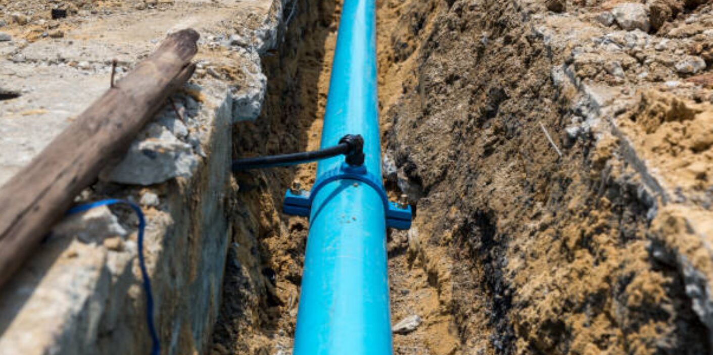 Exposed blue PVC water pipe in dug trench during water line repair service, showing underground plumbing fix in dirt soil