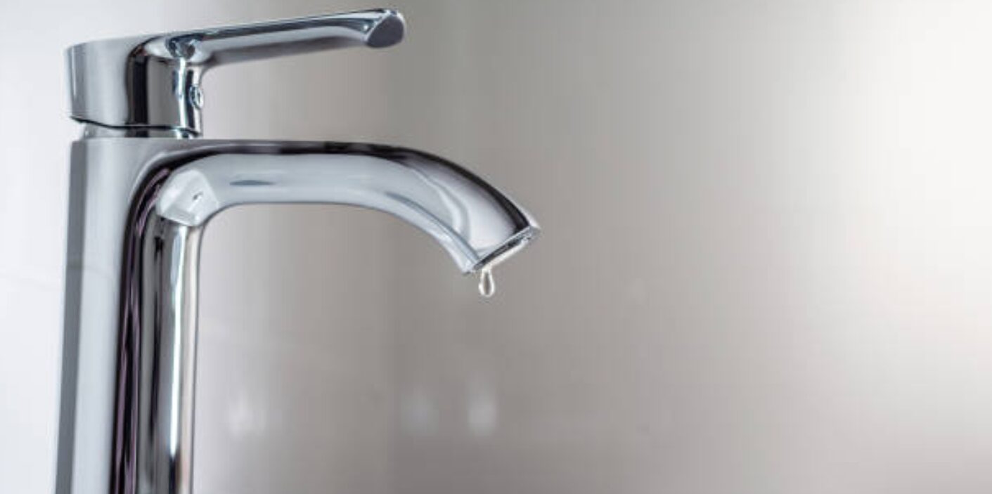 A person trying to stop a dripping sound by tightening a chrome bathroom faucet handle.