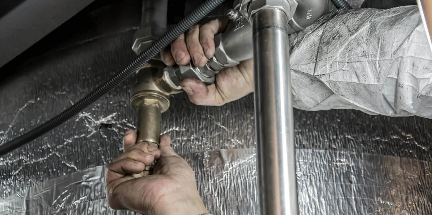 Professional plumber in Knoxville repairing a high-pressure water pipe and brass valve assembly in a residential basement.