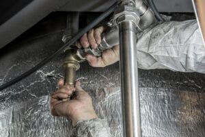 Professional plumber in Knoxville repairing a high-pressure water pipe and brass valve assembly in a residential basement.