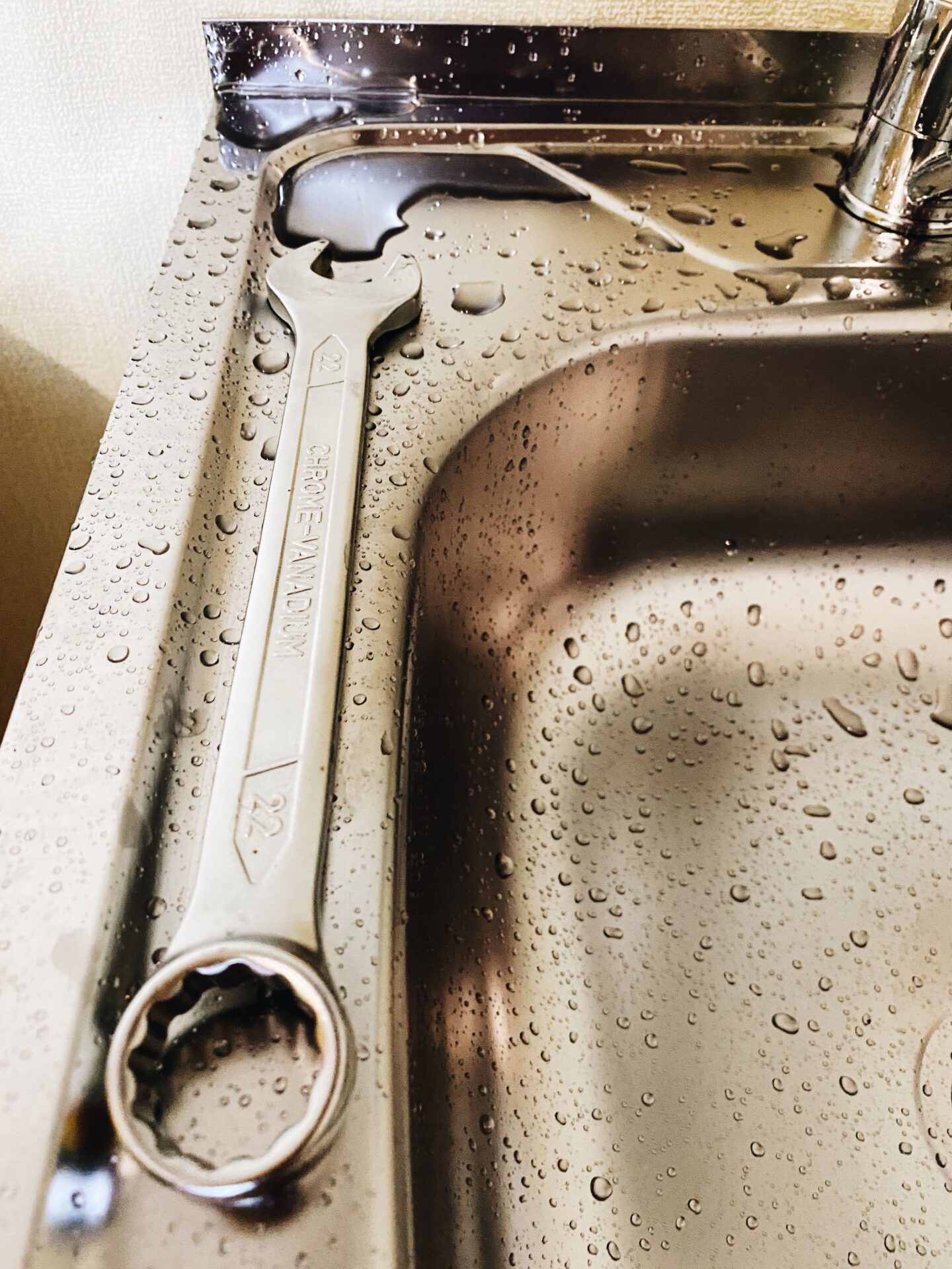 Wrench resting on a wet stainless steel kitchen sink ready for garbage disposal repair