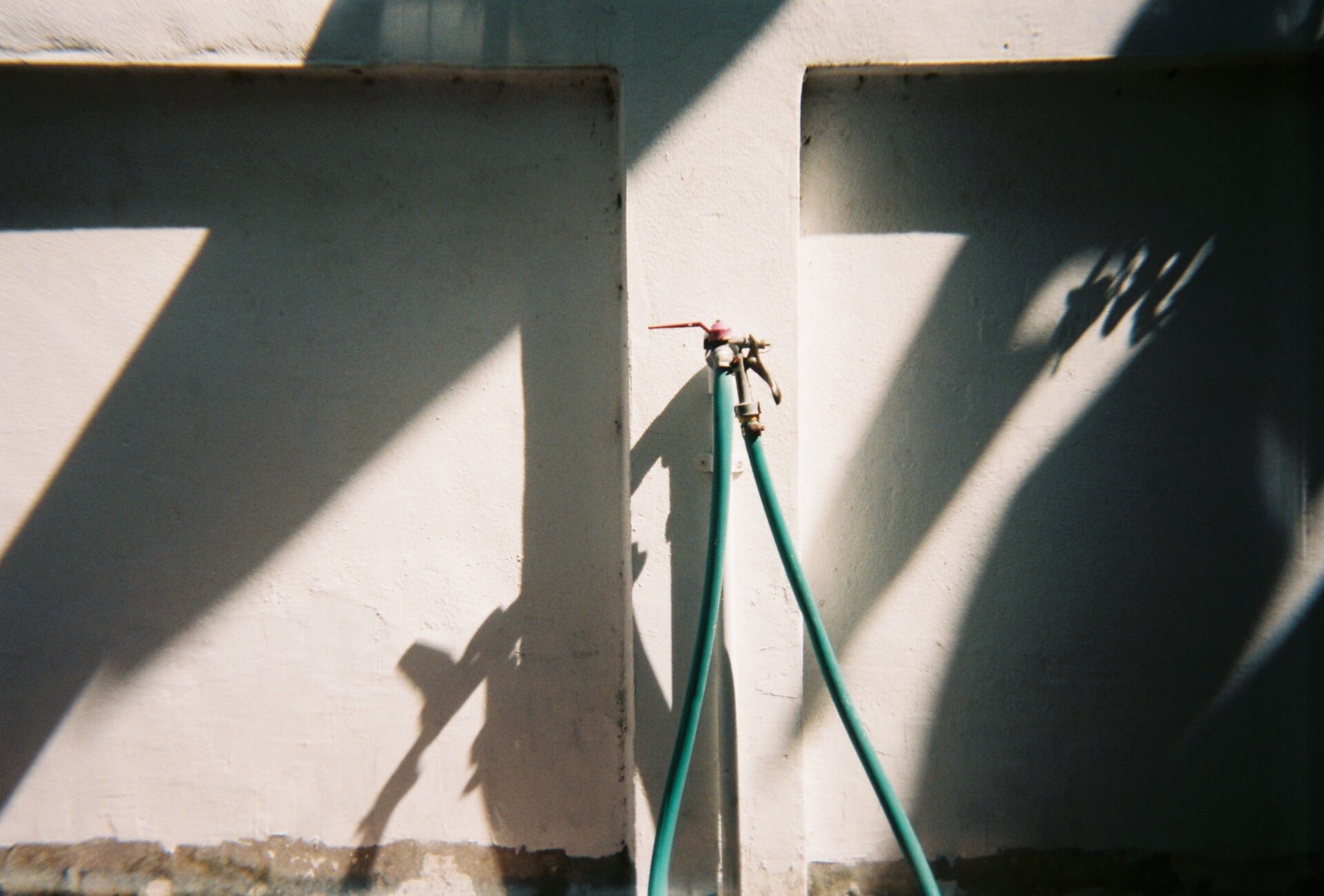 Outdoor hose bib with a garden hose still connected to an exterior wall faucet